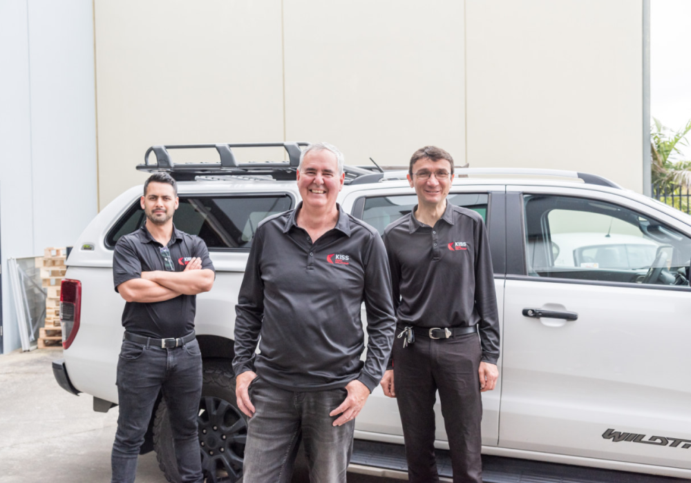 Three men in black KISS Print Solutions shirts standing next to a white SUV